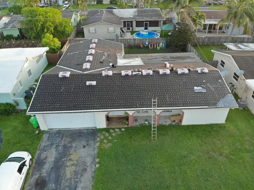Aerial view of a finished dark shingle roof on a single-story South Florida home with a ladder still set against the eave